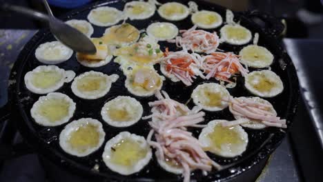 chef de comida callejera poniendo aderezos de mariscos en mini panqueques de mariscos fritos en una sartén de takoyaki de estilo tailandés