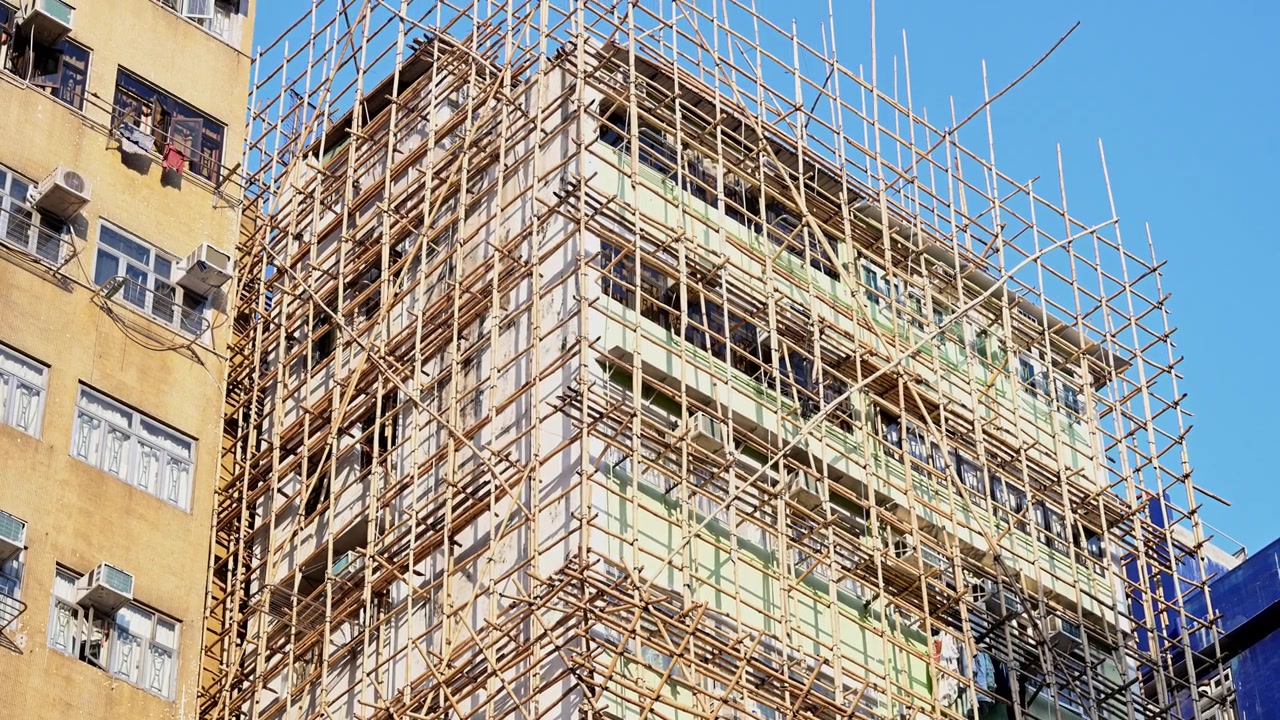Intricate bamboo scaffolding wraps around a residential tower in Hong Kong. Captures the iconic visual of urban growth, renovation, and traditional craftsmanship in the Special Administrative Region.