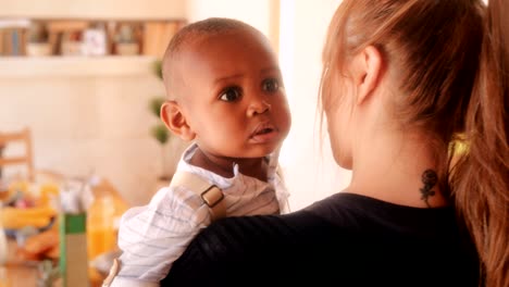 young affectionate mother holding adopted baby son at home