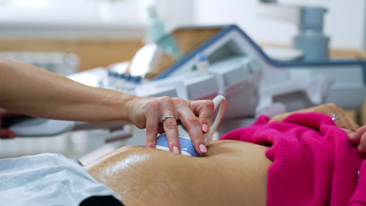 Ultrasound transducer is slowly moved by the pregnant belly of a patient. Intrauterine development of a baby check up.