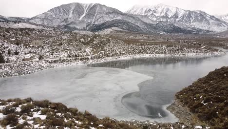 Aerial-view-of-frozen-Lake-Crowley-and-snowy-mountain-and-hill-in-cold-winter