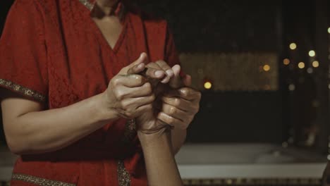 Man-receiving-a-hand-massage-by-a-Hindu-woman-inside-a-traditional-spa,-faceless-people