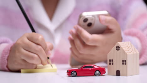 close-up of an individual calculating finances on her car and house loans using a pencil, paper, and a mobile phone as calculator