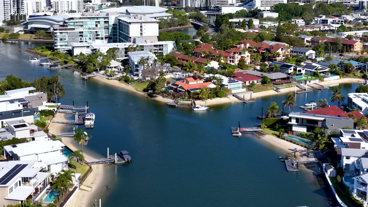 Drone glides above residential canal, modern houses, private docks, bright daylight, smooth camera movement