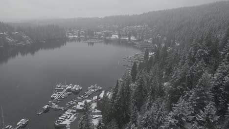 White-Snow-falling-down-over-green-pine-trees-and-marina-with-small-boats-docked-in-Deep-Cove-Bay-in-British-Colombia-on-a-cold-cloudy-winter-day