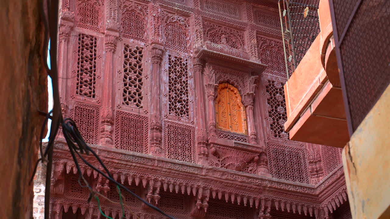 Una ripresa statica dal basso di un'antica Haveli a Jodhpur, che mostra squisite sculture in arenaria rossa, finestre ornate e una piccola porta decorativa gialla in Rajasthan, India.