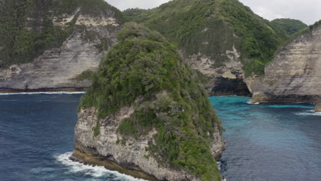 fly by along the steep coast line of nusa penida with remote islands and ocean waves crushing ashore, bali, indonesia