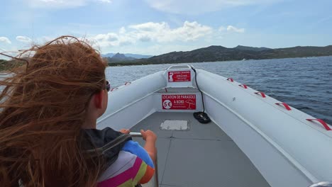 back view of long hair redhead child with sunglasses on motorboat sailing over north corsica sea water for tour toward saleccia famous beach