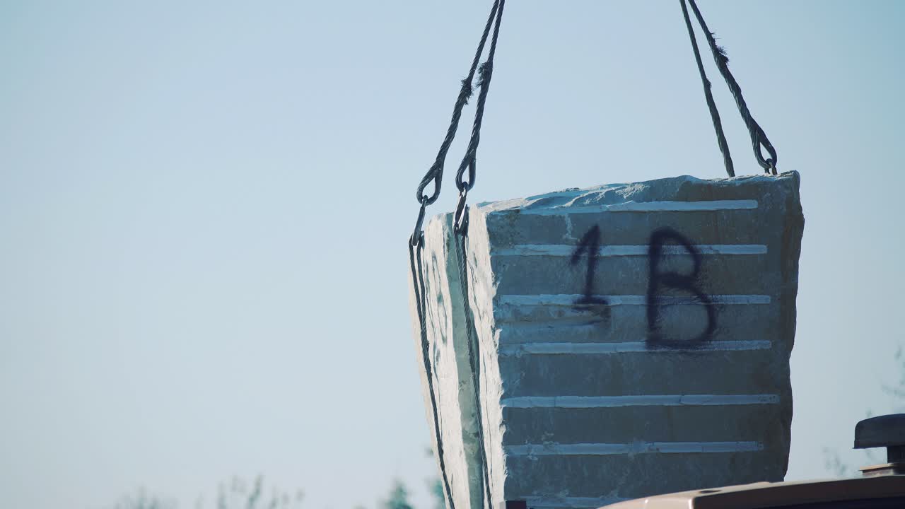 A crane lifts a block of stone from a truck trailer. Sandstone unloading at the plant