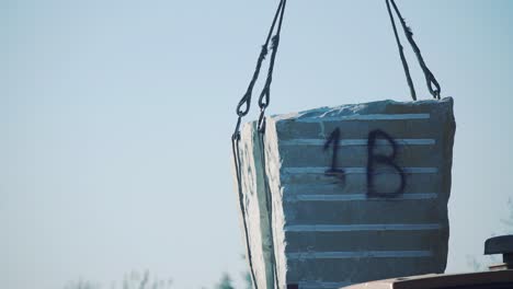a crane lifts a block of stone from a truck trailer. sandstone unloading at the plant
