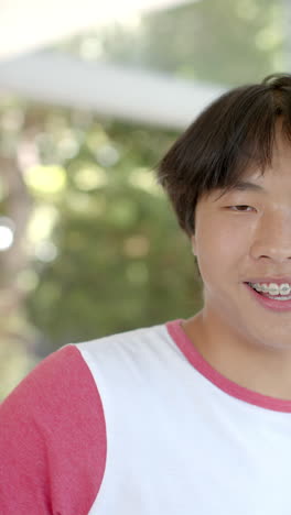 Vertical video: Smiling Asian teenage boy with braces wearing casual shirt at home, looking at camer