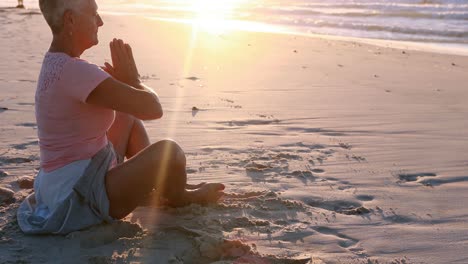 senior woman doing yoga on the beach