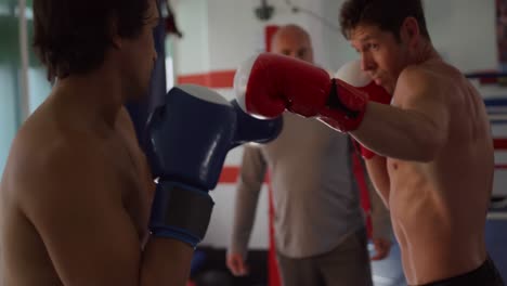 dos hombres caucásicos boxeando con un entrenador en el ring de boxeo