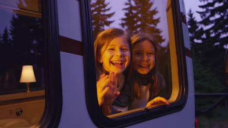 Two Happy Girls Waving from a Camper Van Window at Dusk