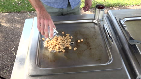 person pours can of beans onto outdoor cooking hot plate, medium shot