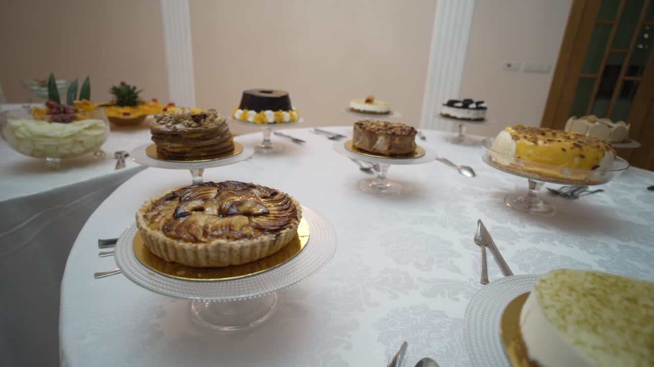 Close-up of a round table filled with a variety of cakes, each beautifully presented on glass stands, creating a tempting display for guests