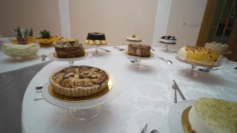 close-up of a round table filled with a variety of cakes, each beautifully presented on glass stands, creating a tempting display for guests