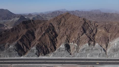 4k:-Rear-top-view-of-UAE-Mountain-range,-Traffic-movement-on-new-Khorfakkan-road-mountains-in-the-background,-Sharjah,-United-Arab-Emirates