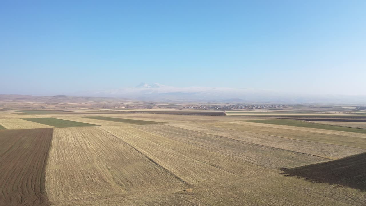Agricultural farmland fields forming patchwork patterns across flat plain, drone moves forward crops, textures, rural landscape, distant mountains