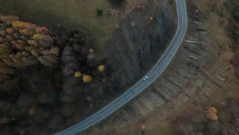 an aerial tilt down drone view of a car driving on a winding road running through a canyon in late autumn