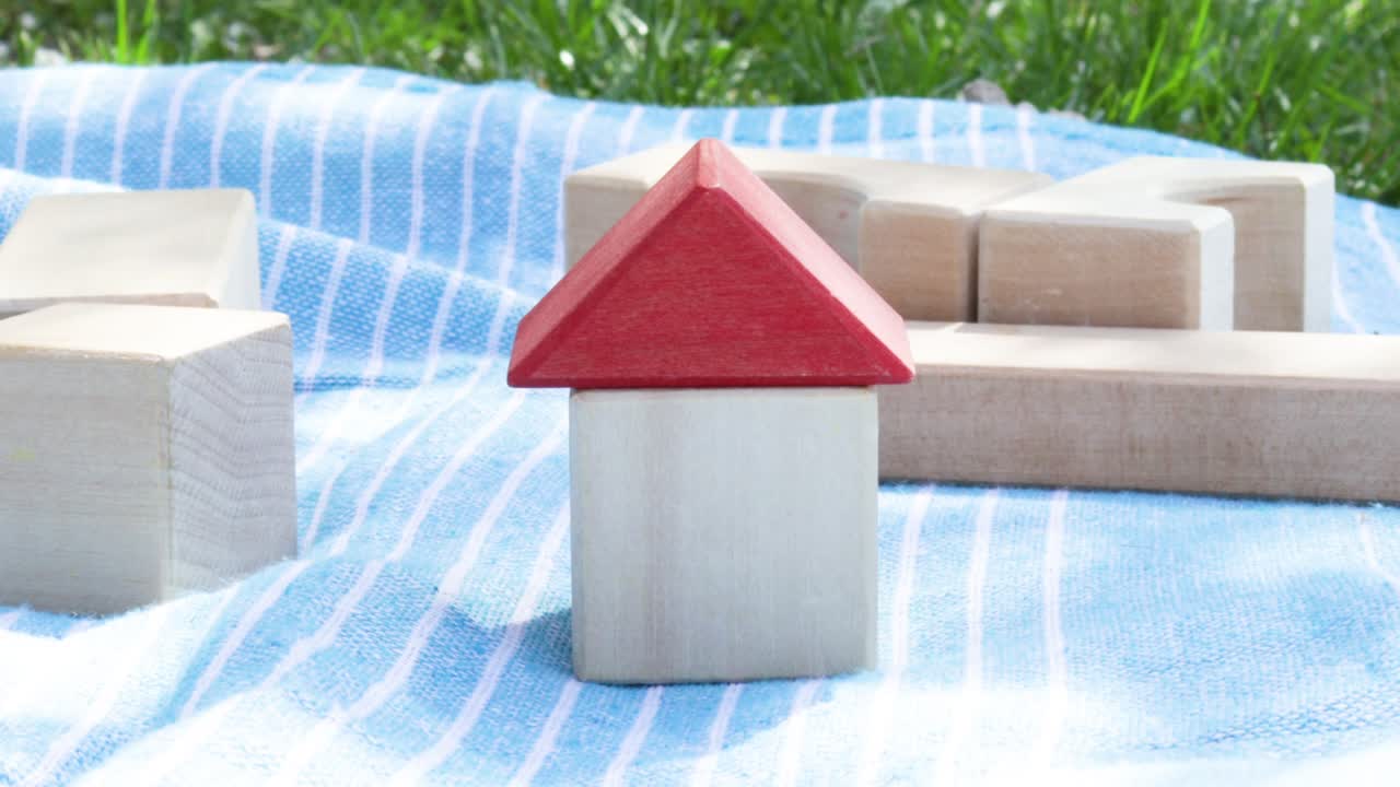 집 보험 개념: 한 손이 나무 에코 큐브 장난감에서 집에 빨간 지붕을 고 있습니다. 공원, 자연 배경에서 담요에 장난감. 은 봄 날.