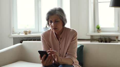 older woman holding cellphone read awful sms, looks shocked