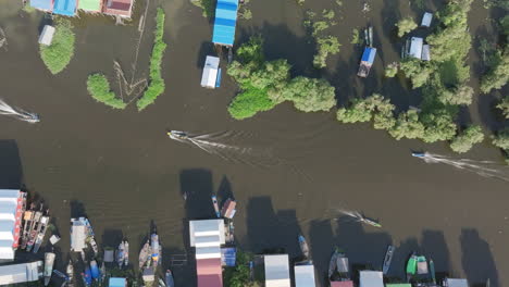 aerial video of tonlé sap boats leaving trails between floating homes and lush green wetlands
