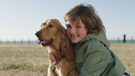 Porträt-Eines-Süßen,-Glücklichen-Jungen,-Der-Fröhlich-Lächelt-Und-Seinen-Hund-Umarmt,-Der-Einen-Sonnigen-Tag-Im-Strandpark-Am-Meer-Genießt