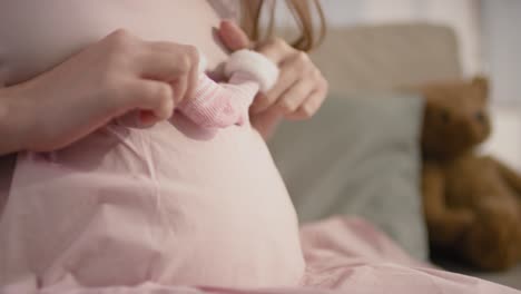 Close-Up-View-Of-The-Fingers-Of-A-Pregnant-Woman-With-Baby-Shoes-Running-Over-Her-Tummy