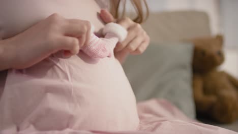 close up view of the fingers of a pregnant woman with baby shoes running over her tummy