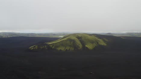 Grüner-Berg-Auf-Schwarzer-Sandlandschaft-Mit-Nebel-In-Island