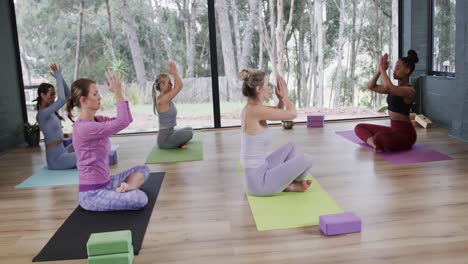 mujeres diversas meditando juntas en esteras en clase de yoga con una entrenadora, cámara lenta