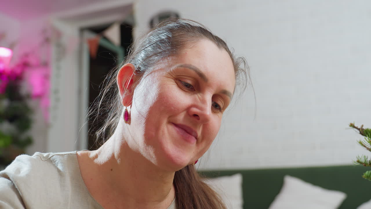 Close view of woman smiling warmly during festive indoor moment, surrounded by soft glowing lights and cozy holiday decor, capturing genuine joyful emotion in bright peaceful living