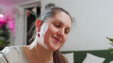 close view of woman smiling warmly during festive indoor moment, surrounded by soft glowing lights and cozy holiday decor, capturing genuine joyful emotion in bright peaceful living
