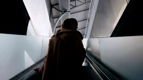 low angle rear view young elegant tourist woman looks back riding modern escalator at a metro station slow motion.