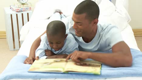 afroamerican little boy and his father reading a book in bedroom