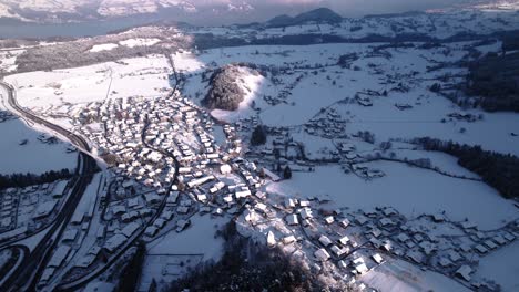 Aerial-view-of-snow-covered-mountains,-villages-and-forests-in-Switzerland-on-a-sunny-winter-day