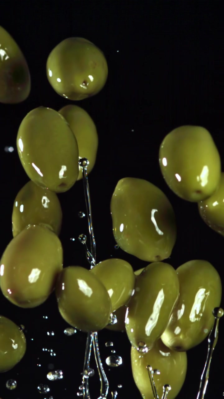 Olive verdi fresche con gocce d'acqua che cadono al rallentatore.