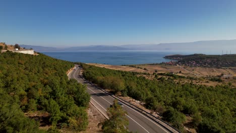 Car-driving-on-curved-road-toward-blue-lake-in-panoramic-landscape-of-Albania