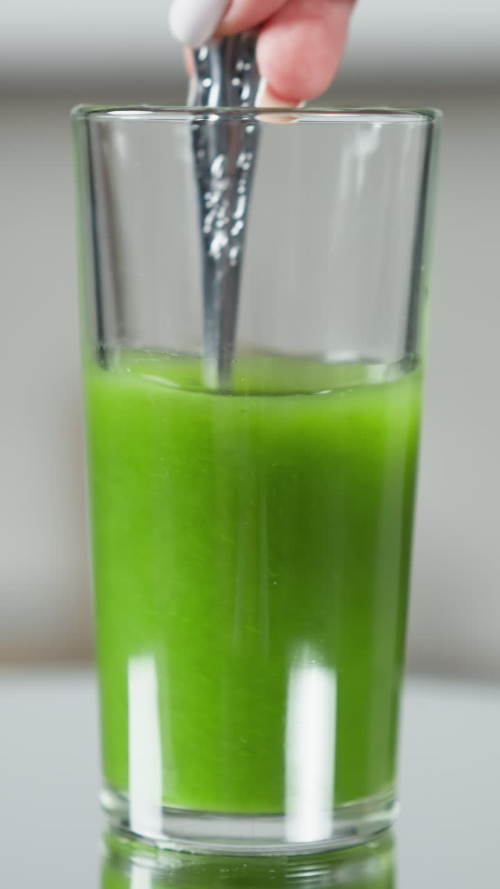 Dito che si immerge in un bicchiere di frullato verde, con un riflesso su un tavolo di vetro
