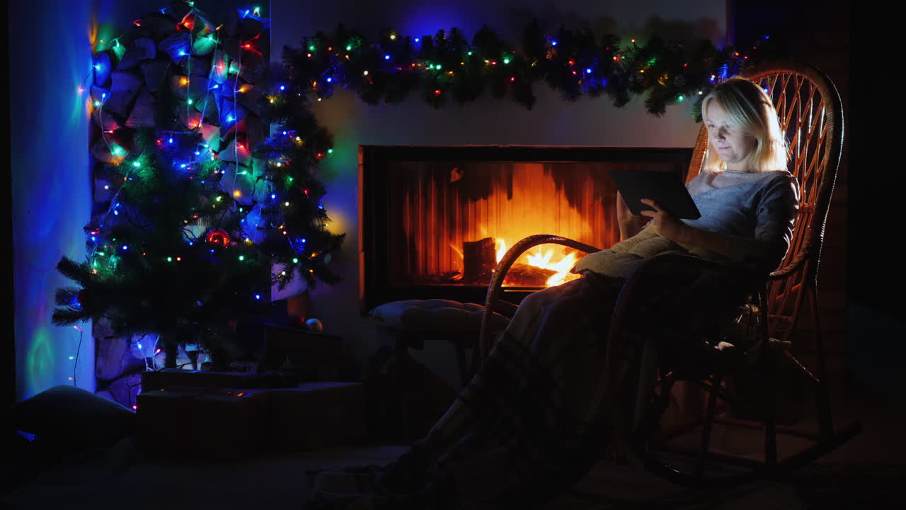 벽난로 옆의 따뜻한 저녁 - 한 여성이 흔들의자에서 태블릿으로 책을 읽고 있습니다.