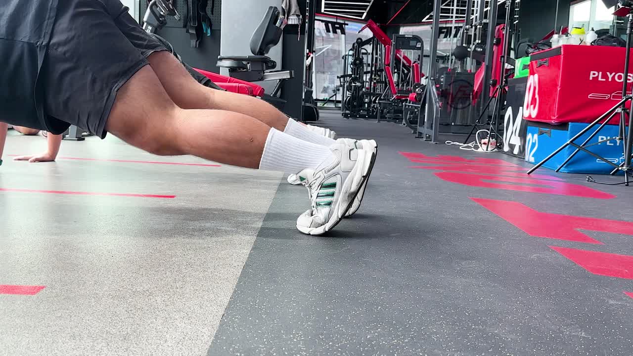 Athletic man does mountain climbers on gym floor, bright lighting, low angle, dynamic movement