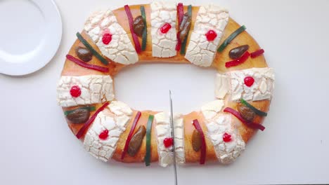 a person cutting a rosca de reyes - three kings bread on a white table