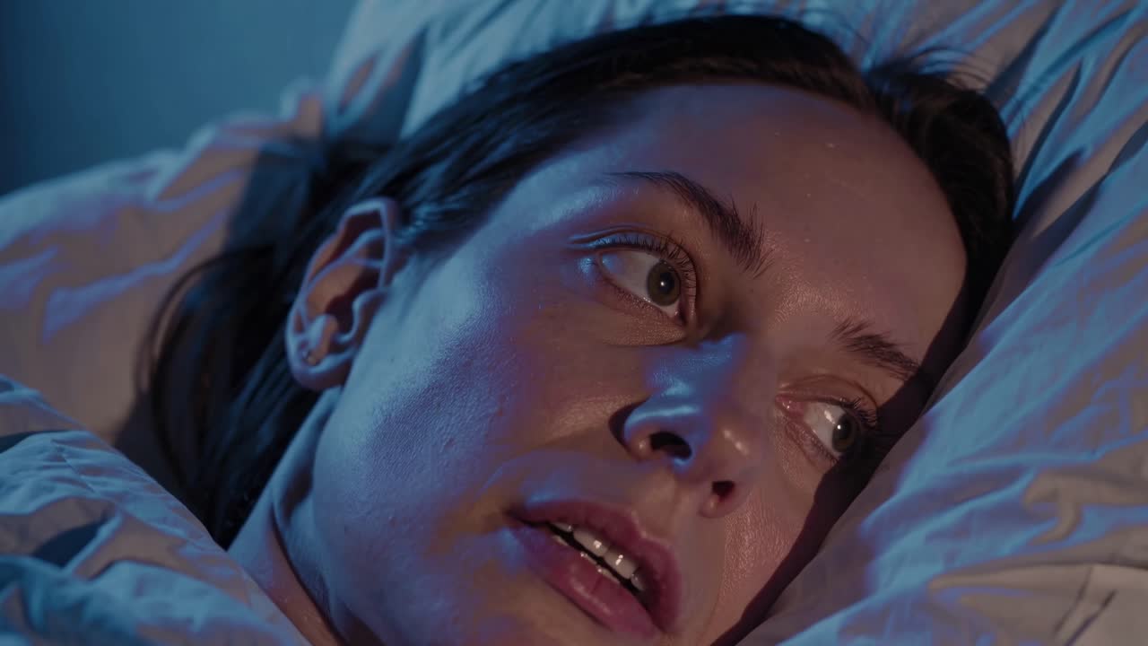 Close-up video shot of a person lying in bed, illuminated by blue light, capturing a contemplative