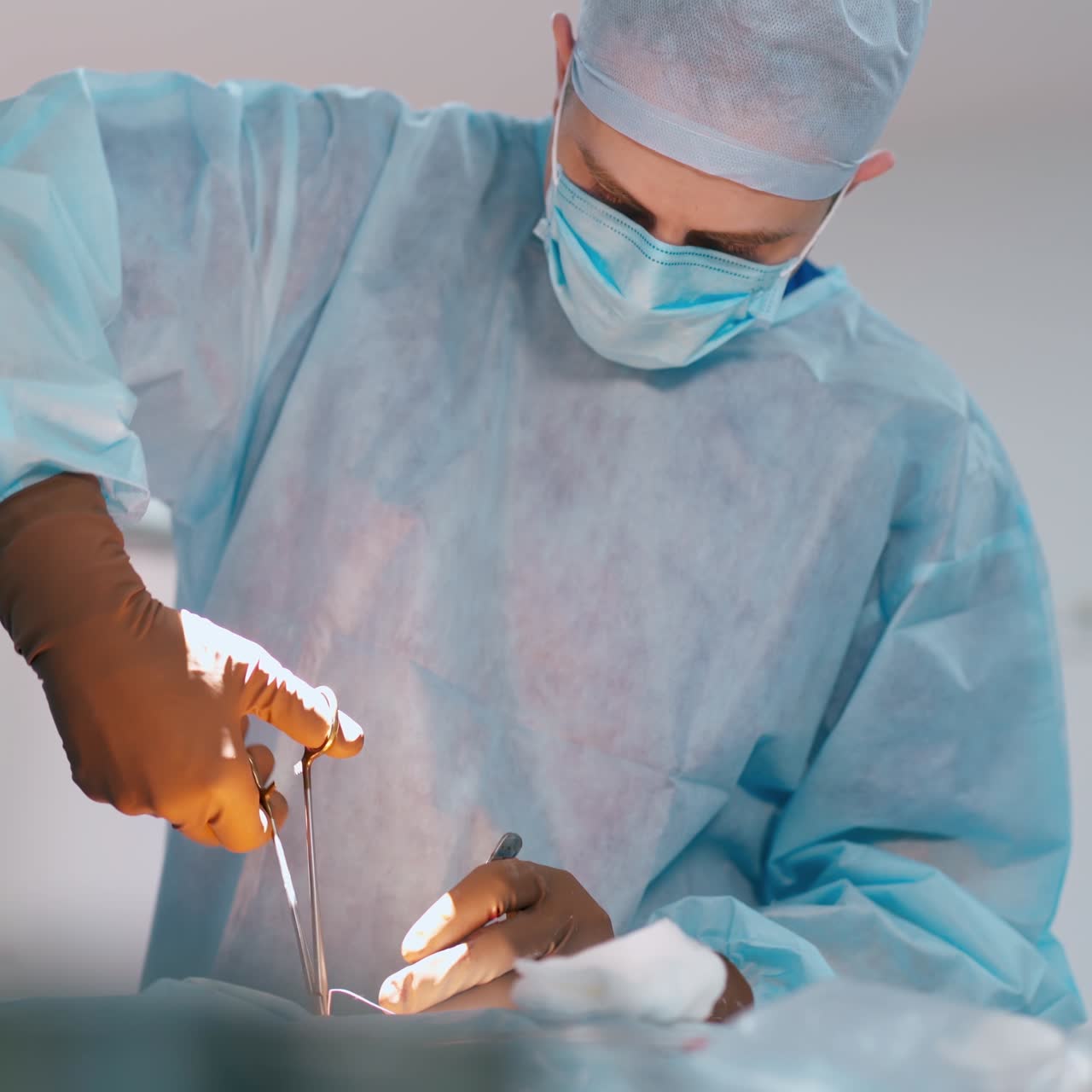 Successful doctor finishing a surgery. Professional surgeon in medical uniform and mask performing an operation in a modern hospital.