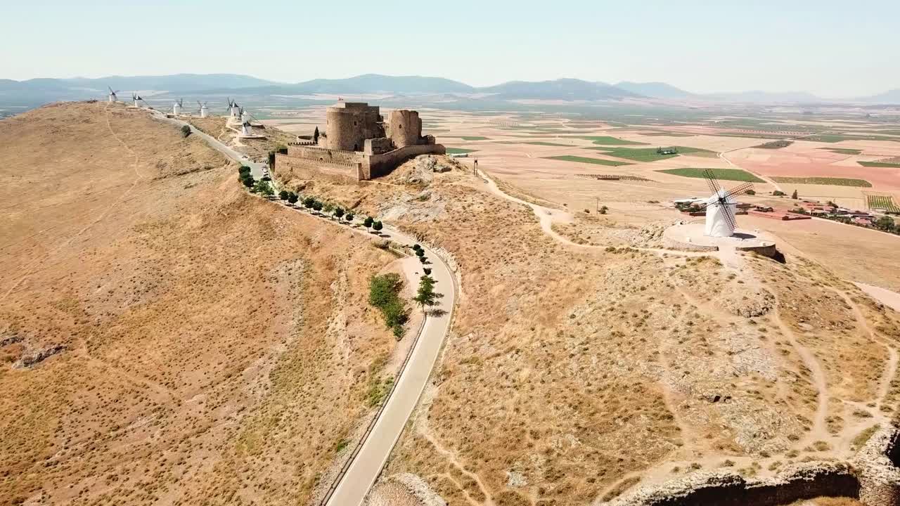 A stunning view of Molinos de Viento de Consuegra in Spain, featuring historic windmills and a medieval castle atop a hill surrounded by picturesque fields and landscapes