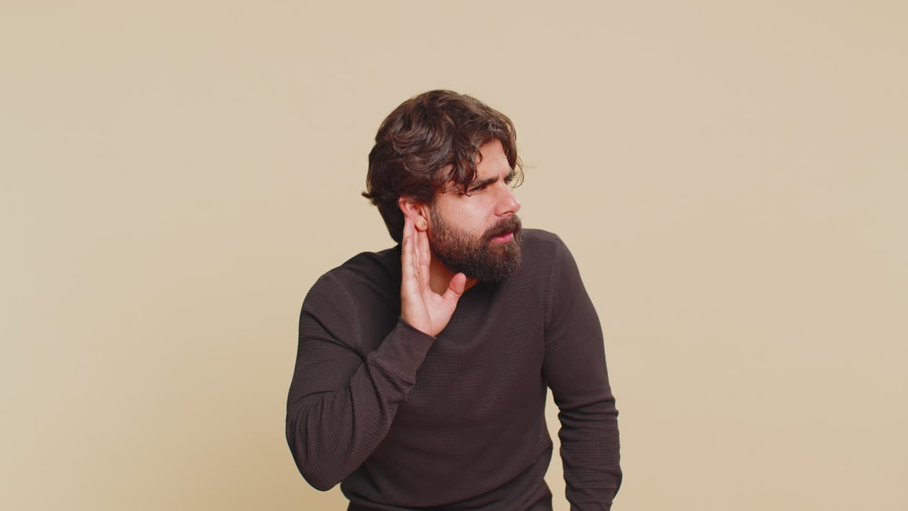 Young lebanese man guy trying to hear you looking confused and frowning against beige background
