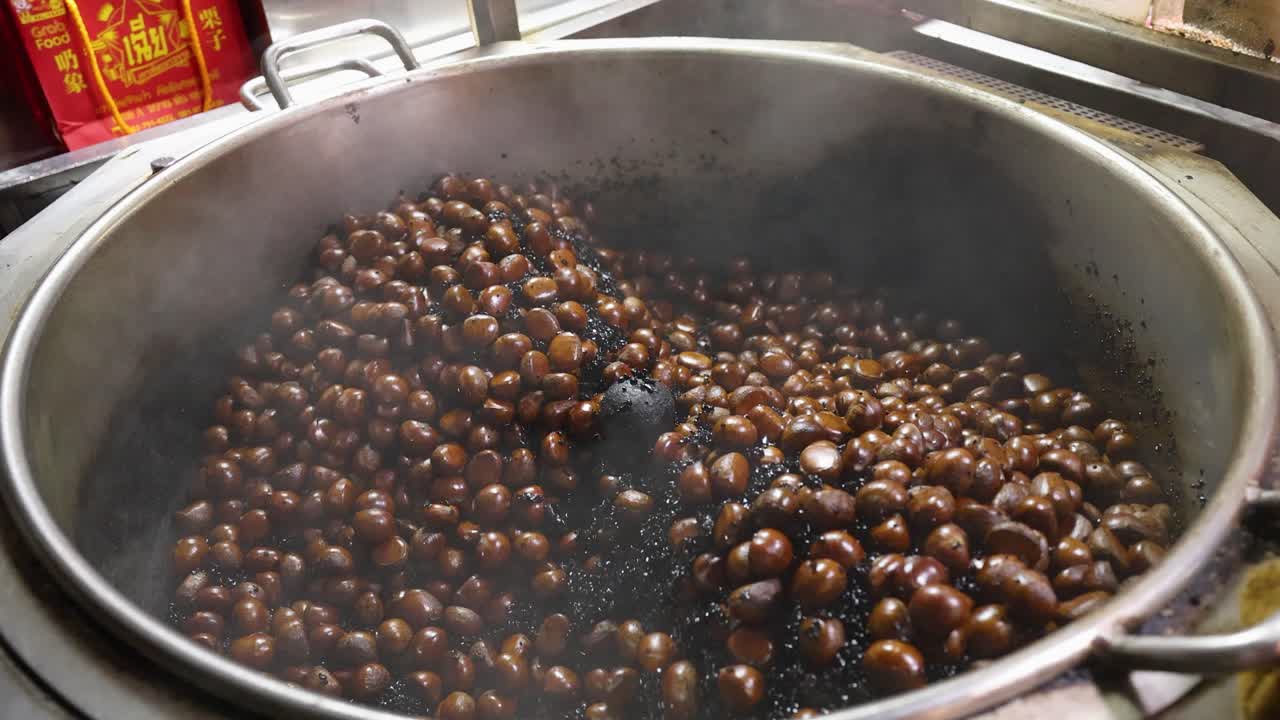 Chestnuts roasting in a steaming metal pan, street food scene, natural lighting, close-up view