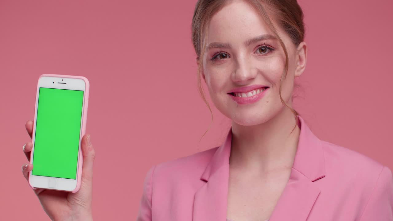 Ragazza estremamente felice e soddisfatta che mostra uno schermo verde sullo smartphone. Ragazza naturalmente bella che posa in studio con un outfit elegante, mostrando lo schermo verde alla fotocamera. La ragazza apprezza la nuova app mobile. Telefoni.