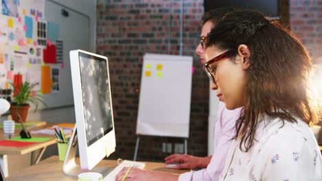 Businesswoman-sitting-with-coworker-while-working-on-computer